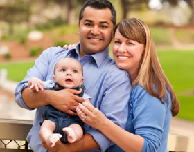 A mixed race couple with a baby standing outside together