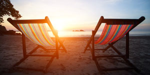 Two chairs on the shoreline of the beach facing the ocean with view looking towards the sun raising